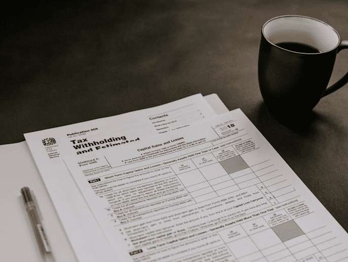 Two people reviewing documents at a desk with a laptop and yellow mug. A calendar icon shows the number 15. Bookshelves are in the background.